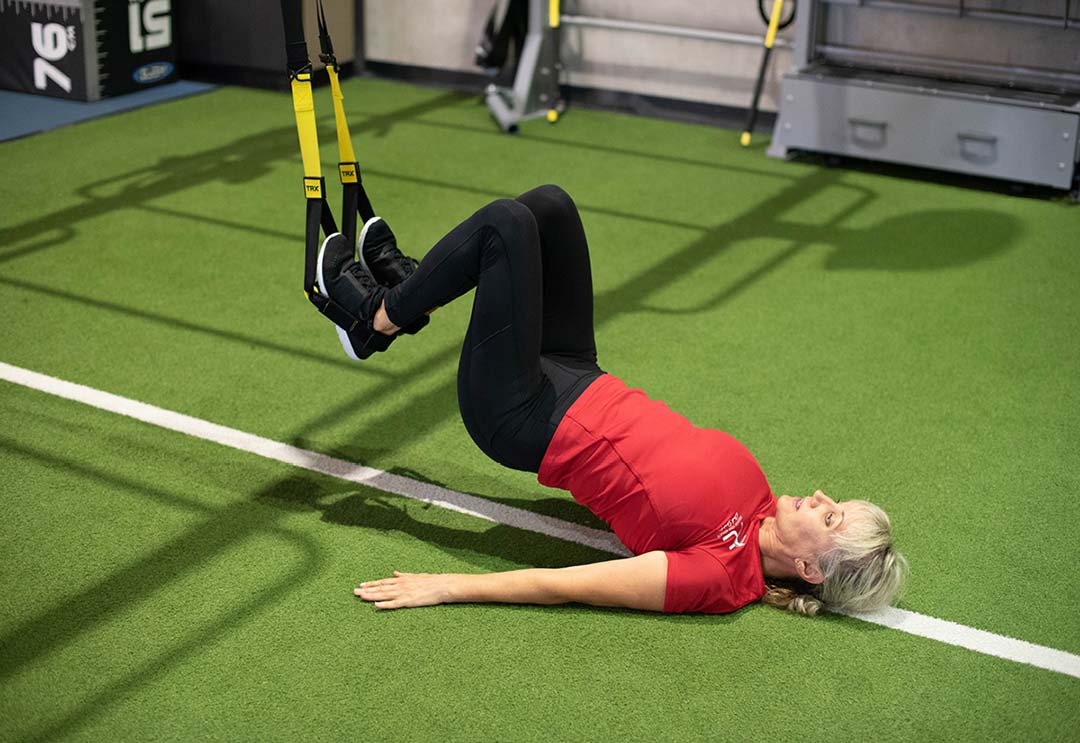 Woman lying on her back doing a TRX hamstring exercise