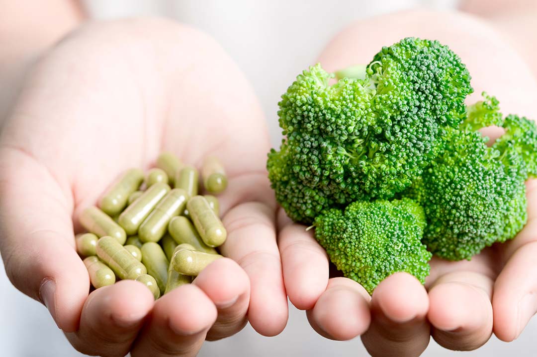 I woman holding supplements in one hand and broccoli in the other hand