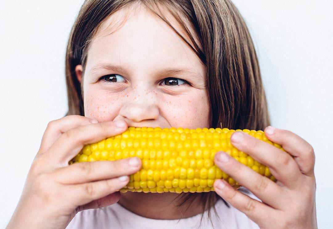 Little girl around 9 years old eating corn on the cob