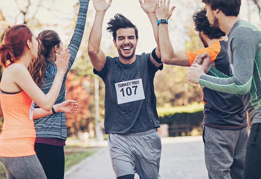 A man finishing a Turkey Trot race giving high-fives to his friends