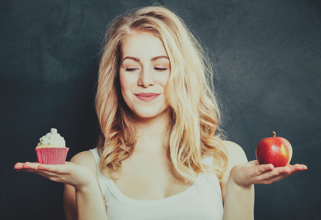A woman holding an apple in one hand and a cupcake in the other