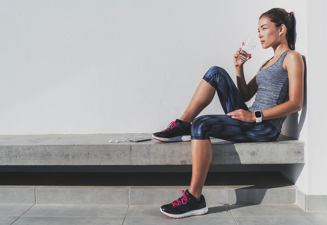 Woman sitting down drinking water after a workout at the gym
